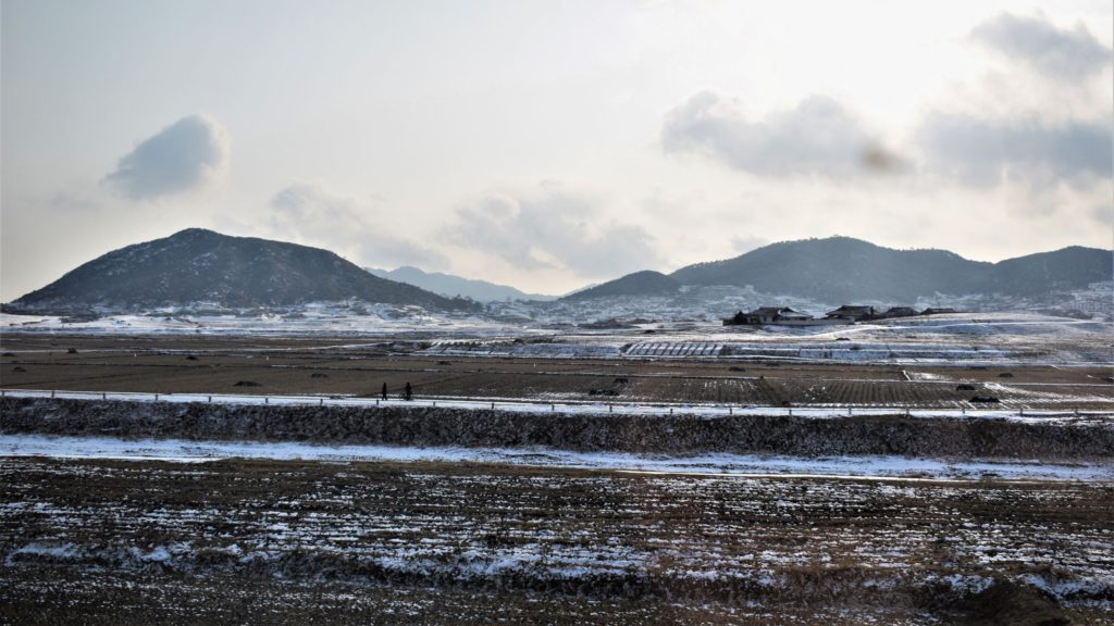 barren rice fields covered in snow in front of traditional Korean farm houses, Korean countryside, DPRK