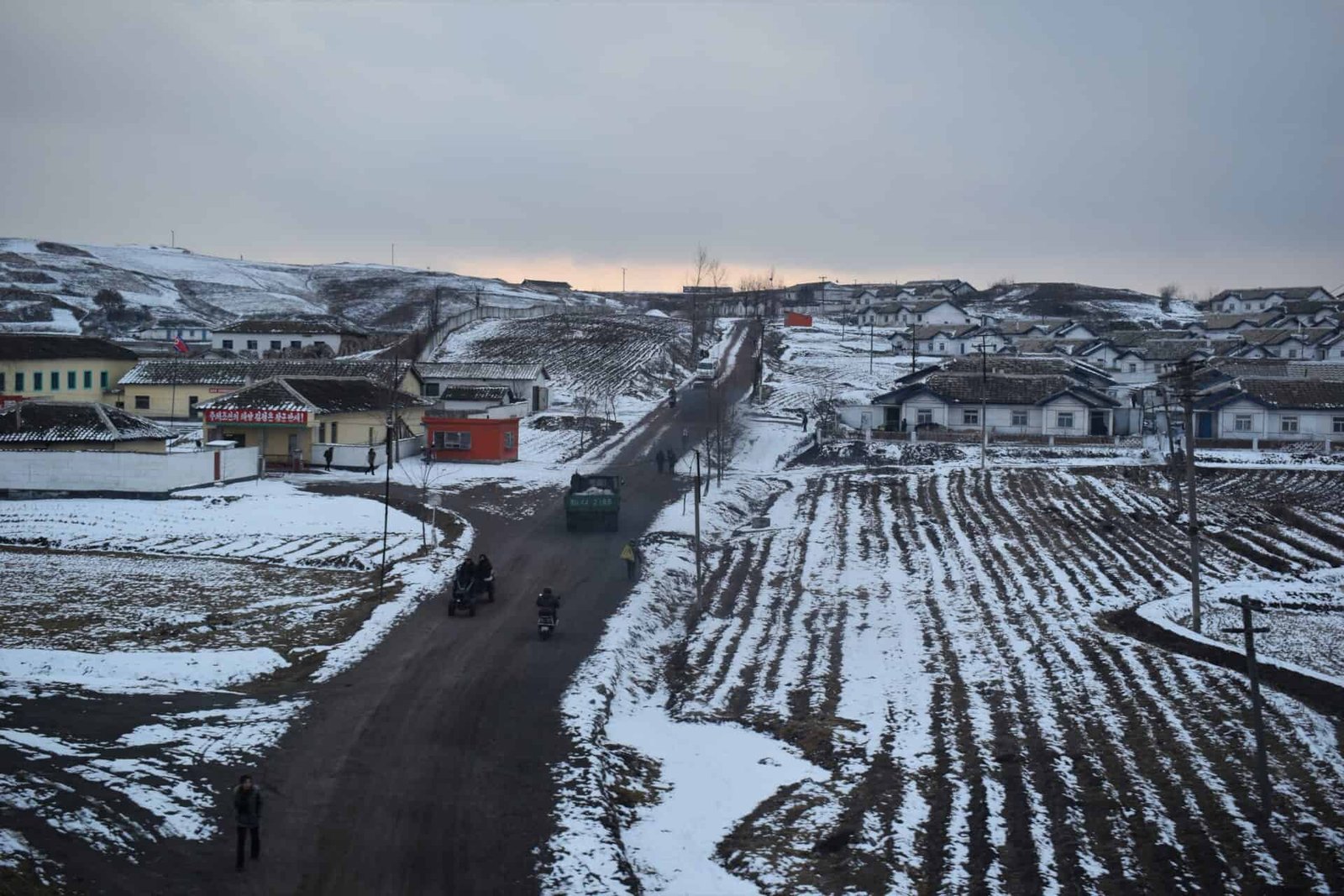dirt road leading through a North Korean village lined by snow-covered fields