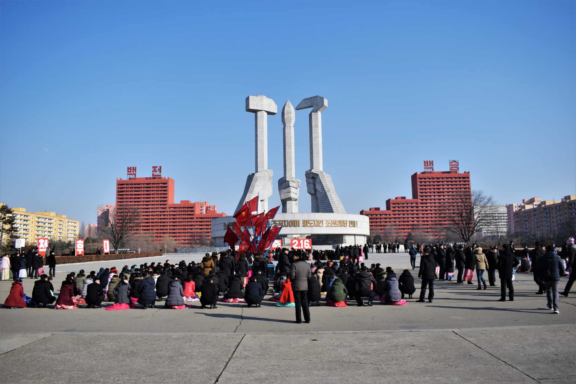 students sit down in front of a massive communist monument in North Korea's capital Pyongyang