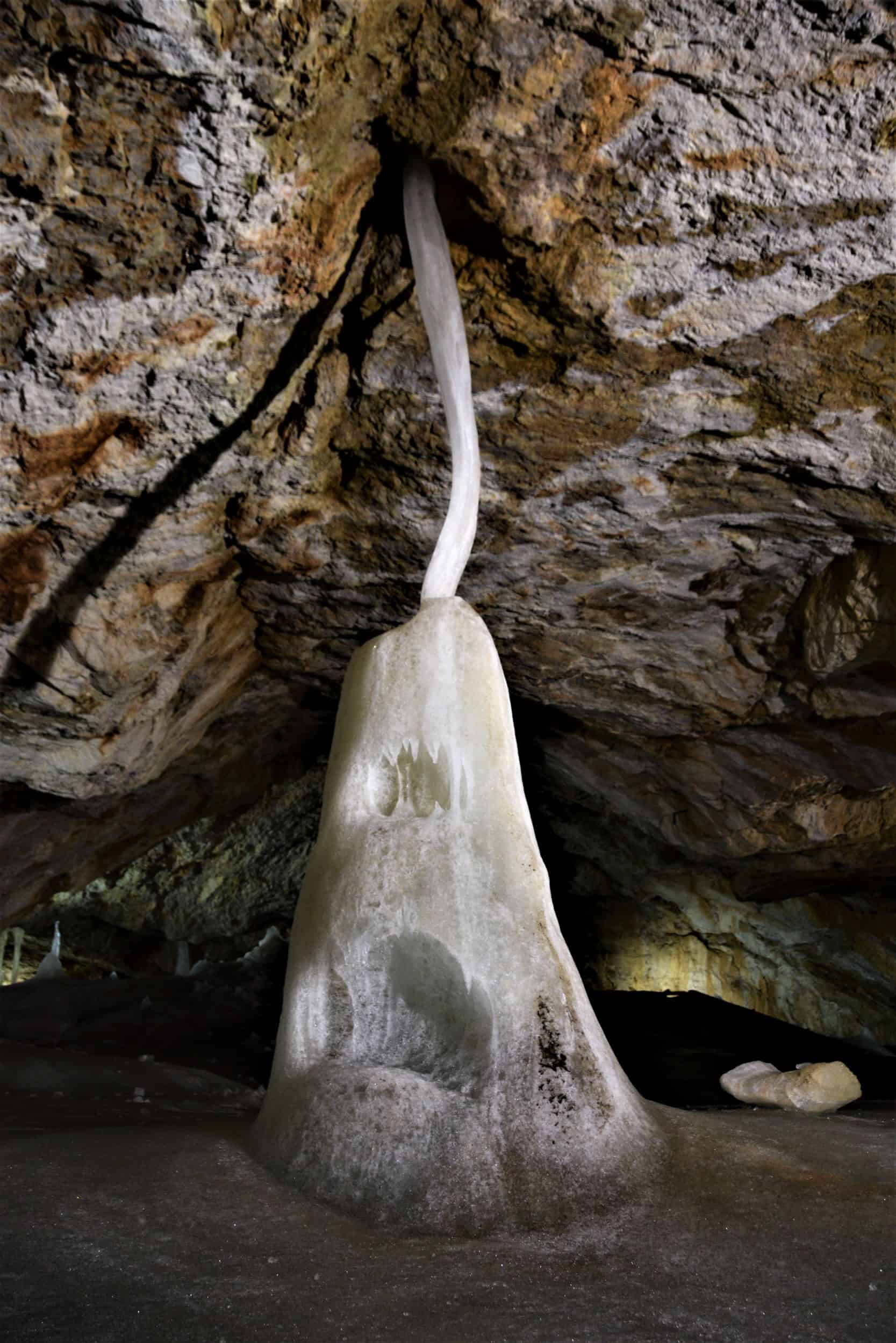 a ghostly looking ice mount connects to the ceiling via a thin frozen ice strand (front view), Dobsina Ice Cave, Slovakia