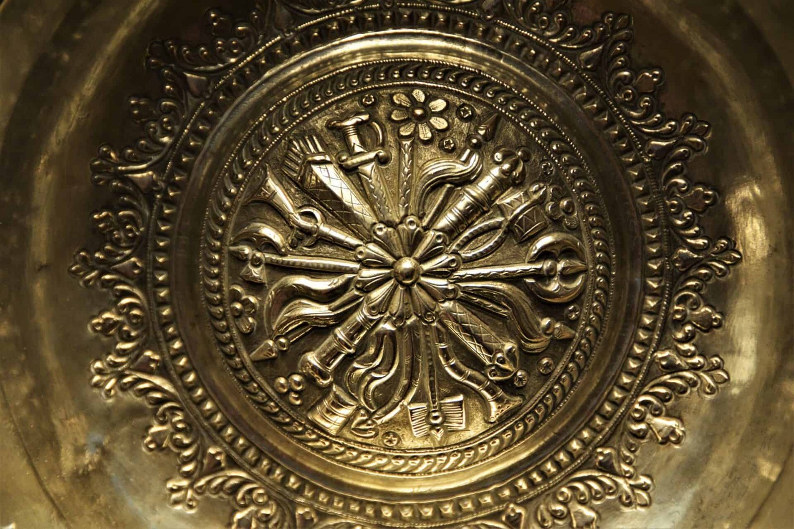 richly decorated silver plate using the repoussage methode boasting different arms, circular patterns, and a flower in the middle