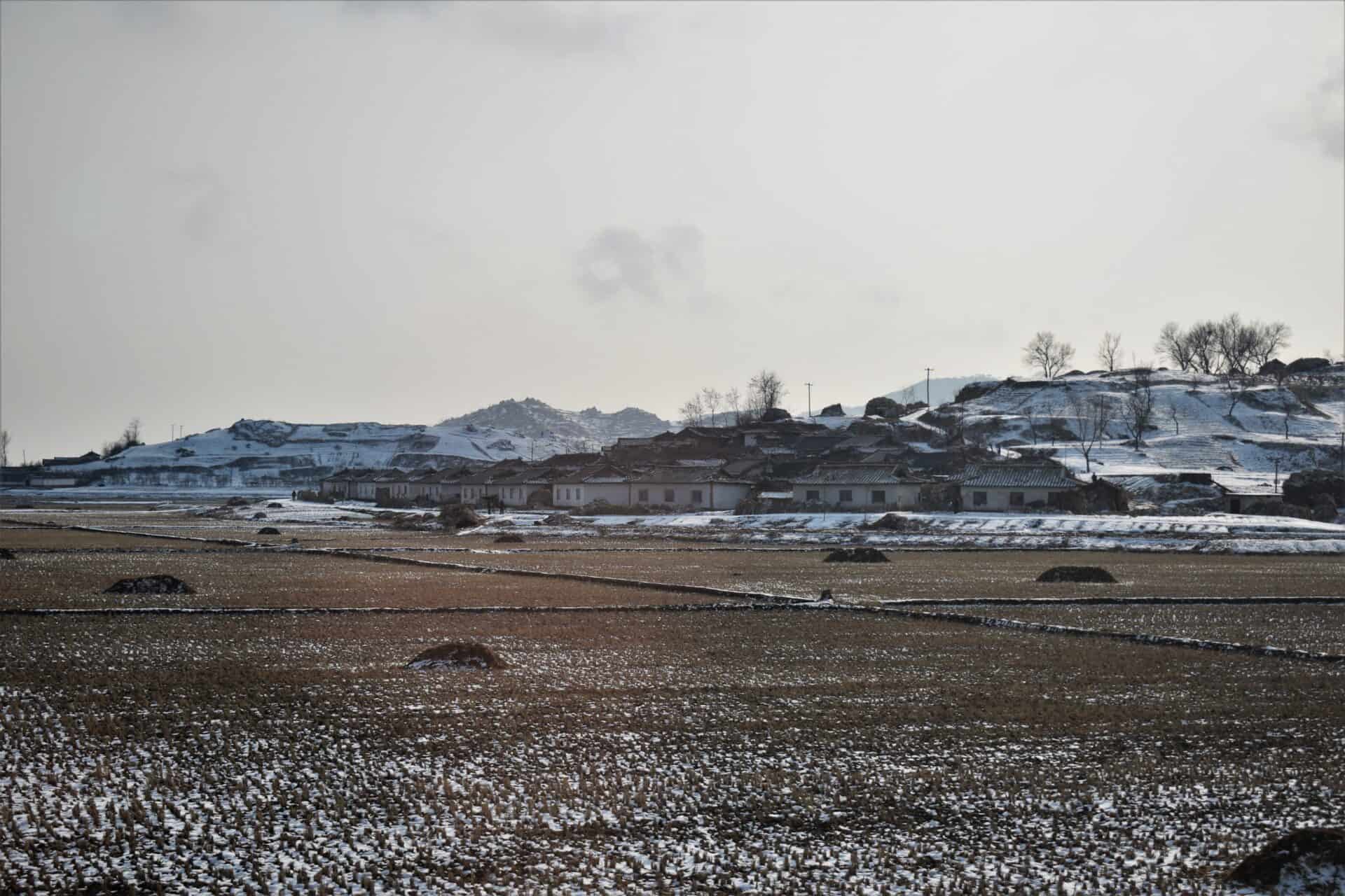 North Korean village hugging a snow-covered hill surrounded by barren fields