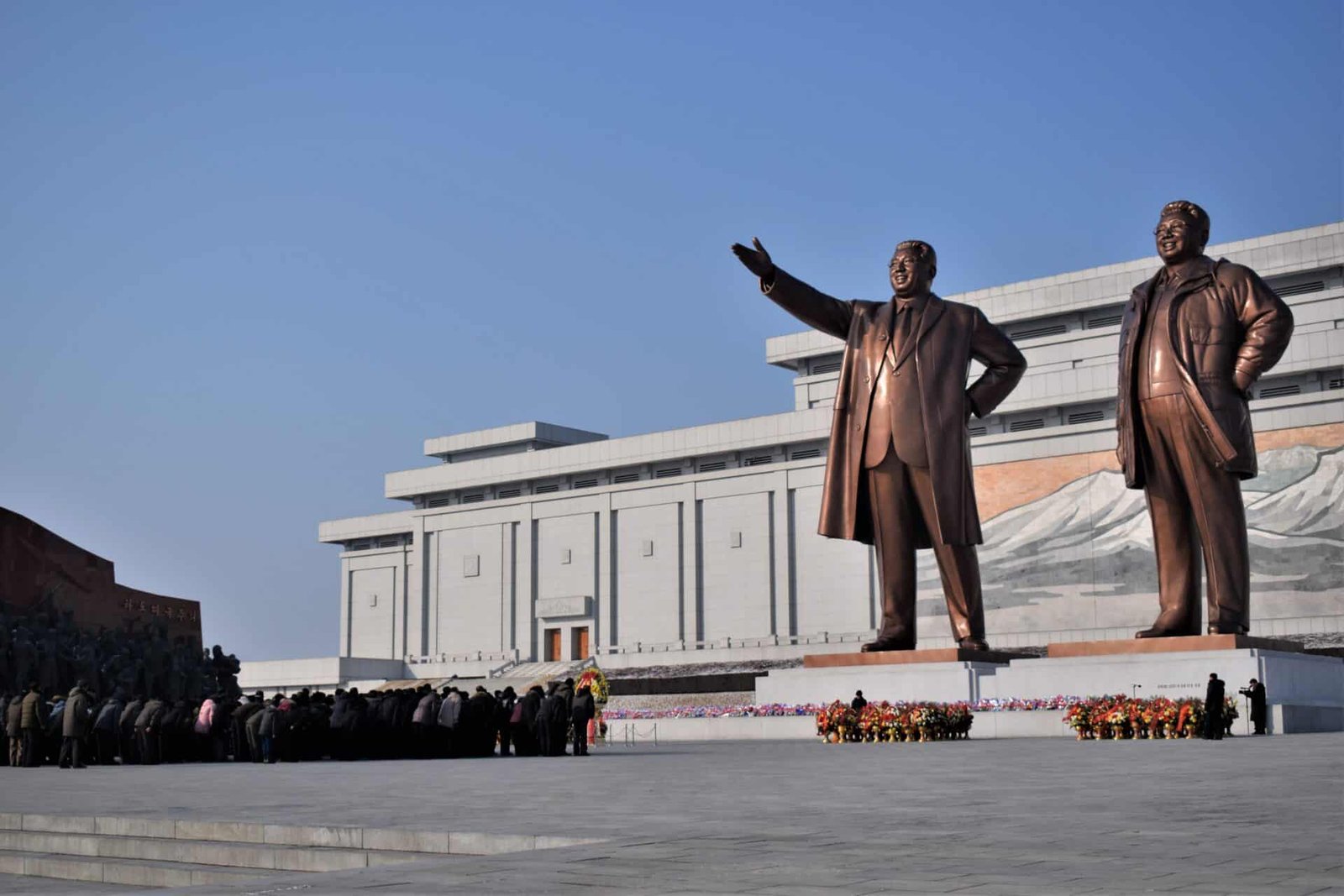 people bowing down and paying their respect in front of two giant bronze statues of former North Korean leaders Kim Il-sung and Kim Jong-il