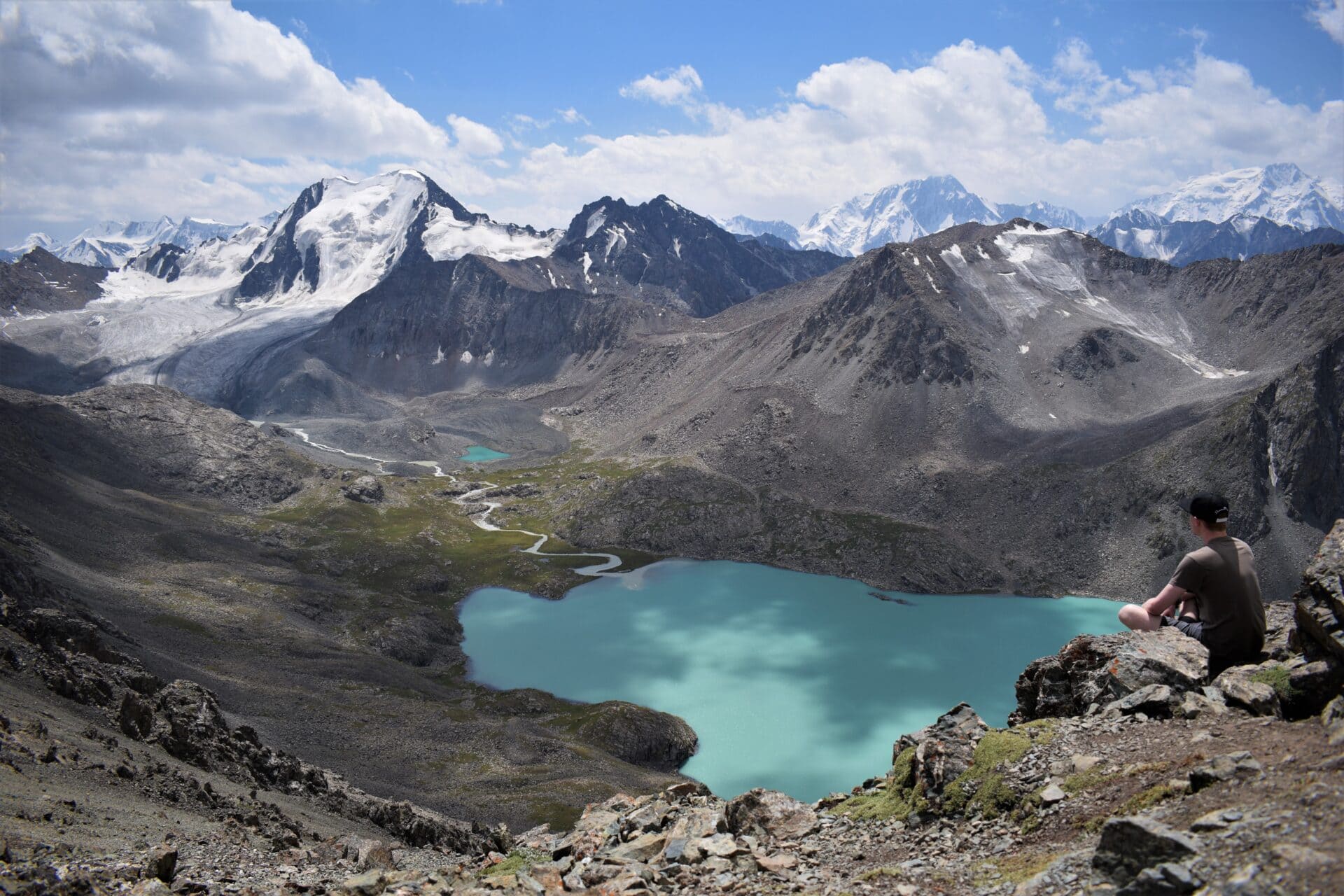 a man sitting on a rocky peak overlooking the turquoise waters of an alpine lake framed by majestic, snow-capped peaks