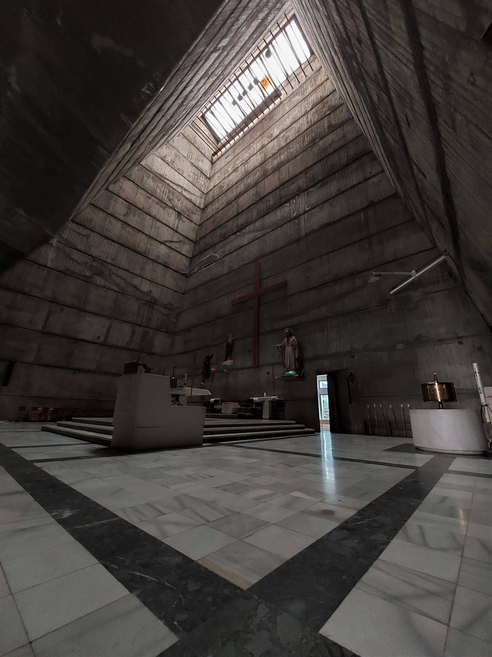 light beams fall through a skylight onto the altar of a catholic church built in the brutalist style