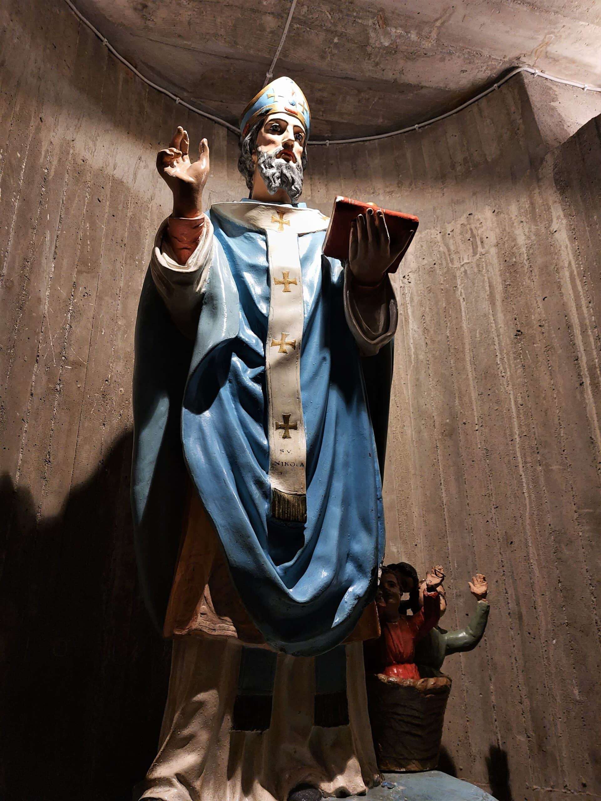statue of a priest in blue robes reading from the bible