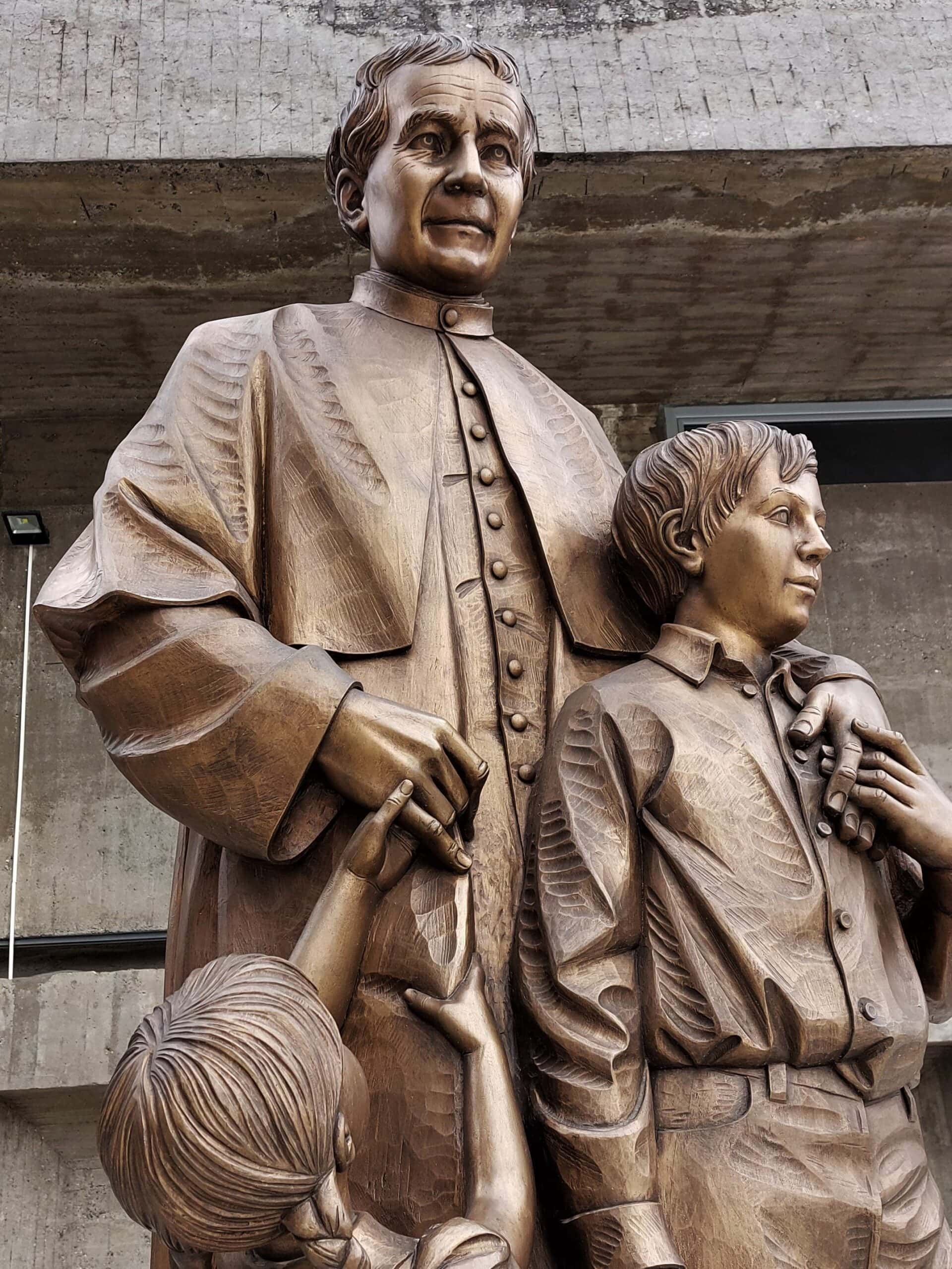 bronze statue of a priest holding a young boy, while a youg girl pulls his other hand
