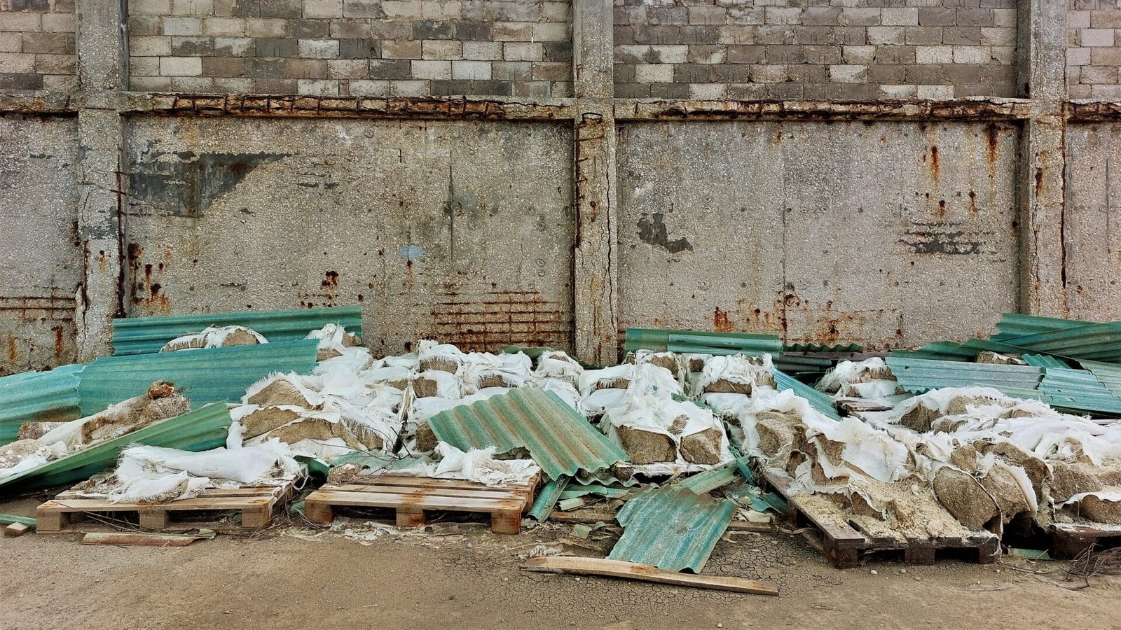 a pile of green corrugated sheet in front of a concrete wall