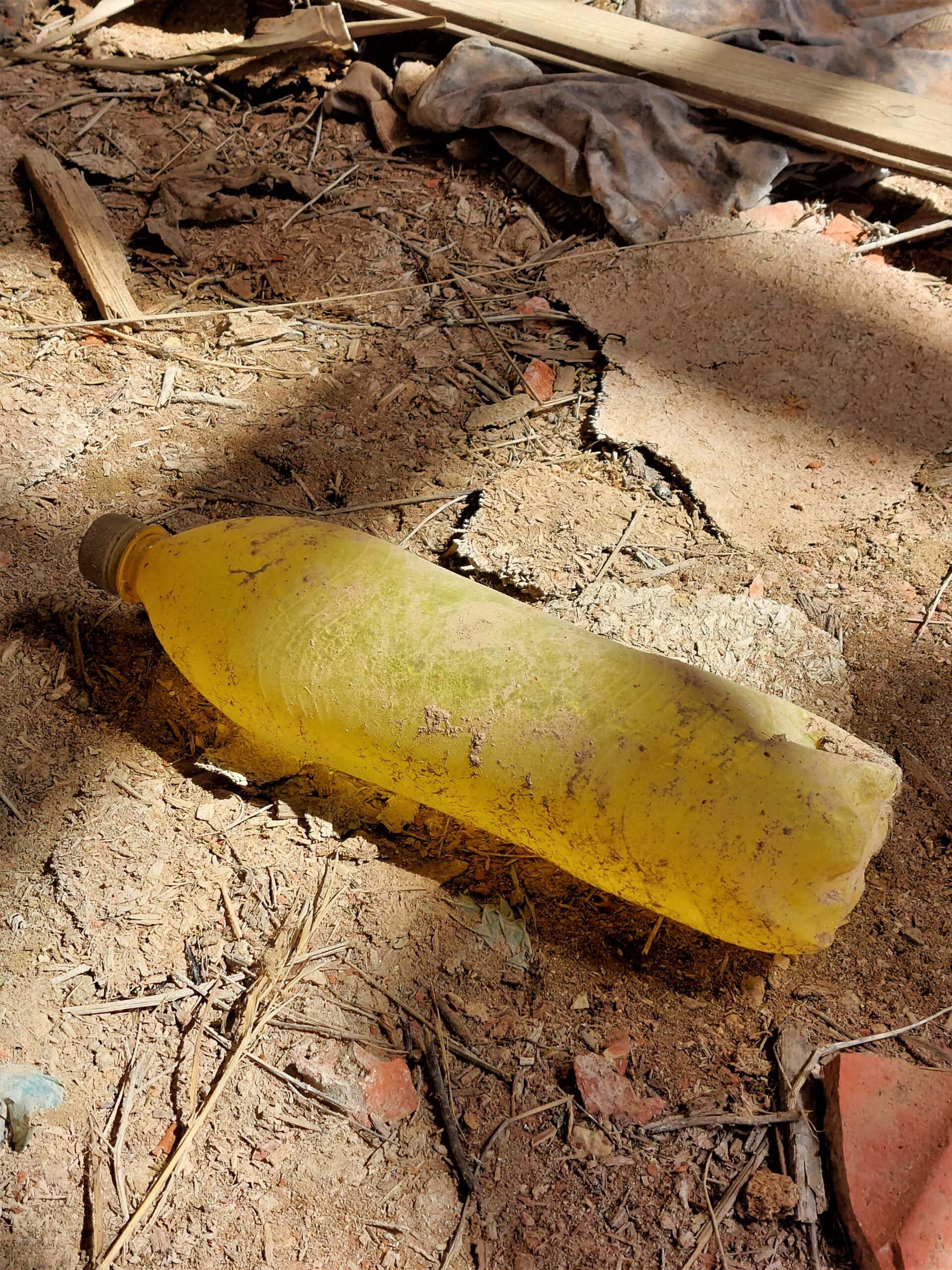 a yellow bottle lies on a dirt floor