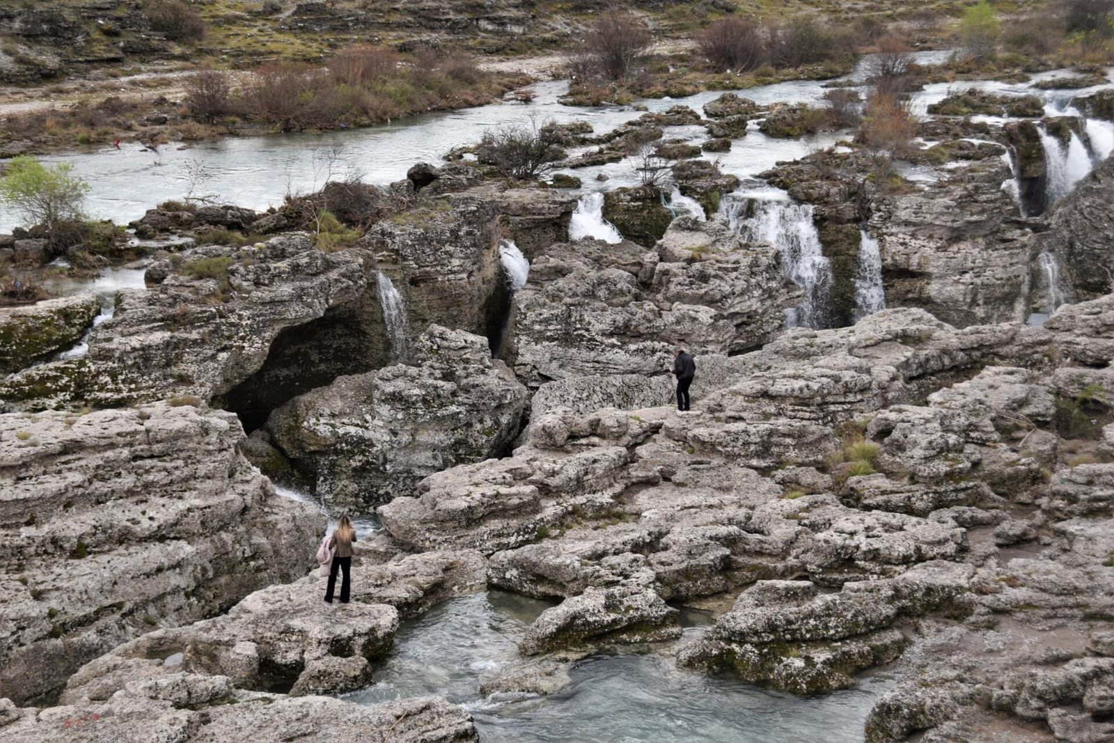two people stand at the ede of a canyon created by a rushing river