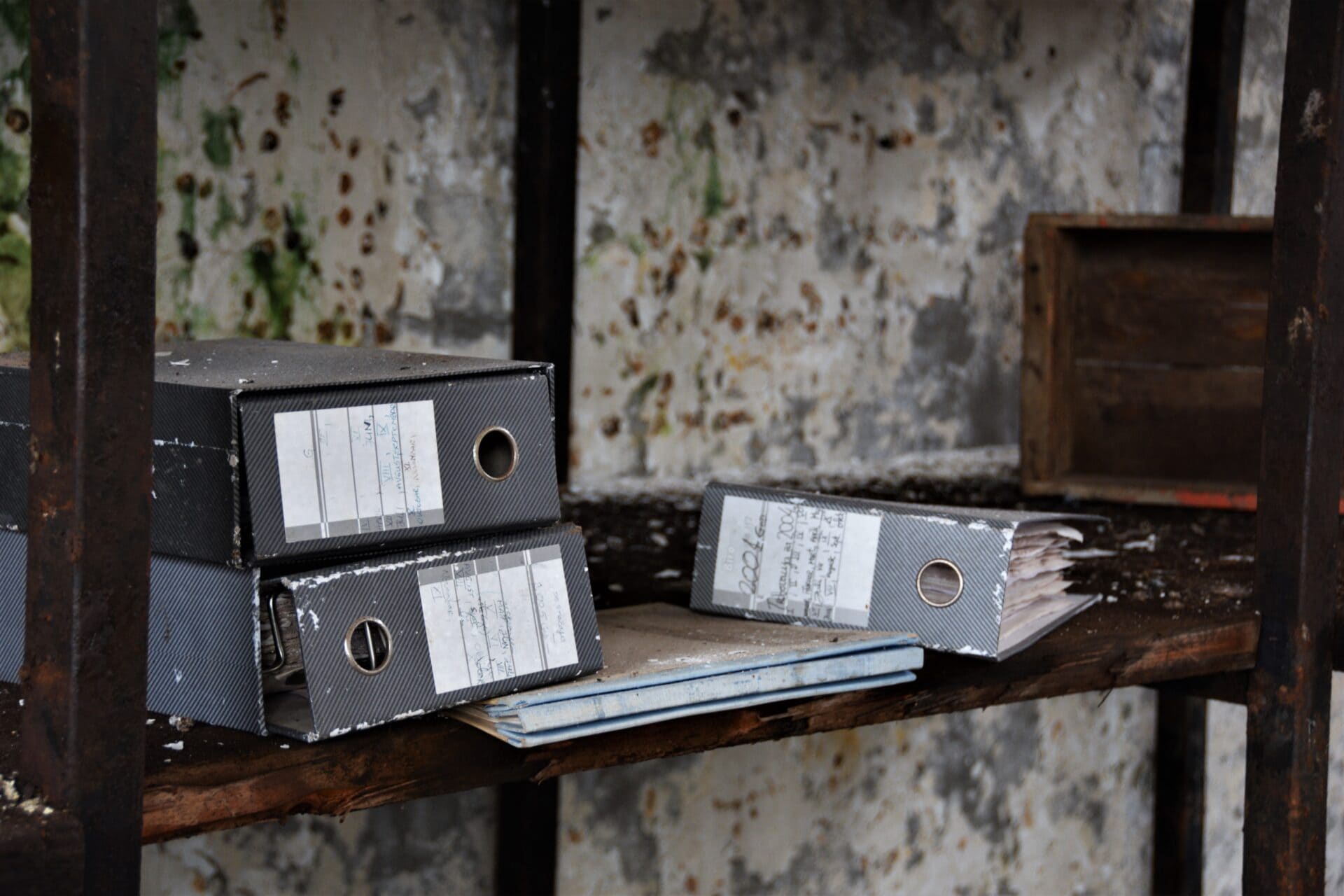 grey folders lying in a rotting, wooden shelf