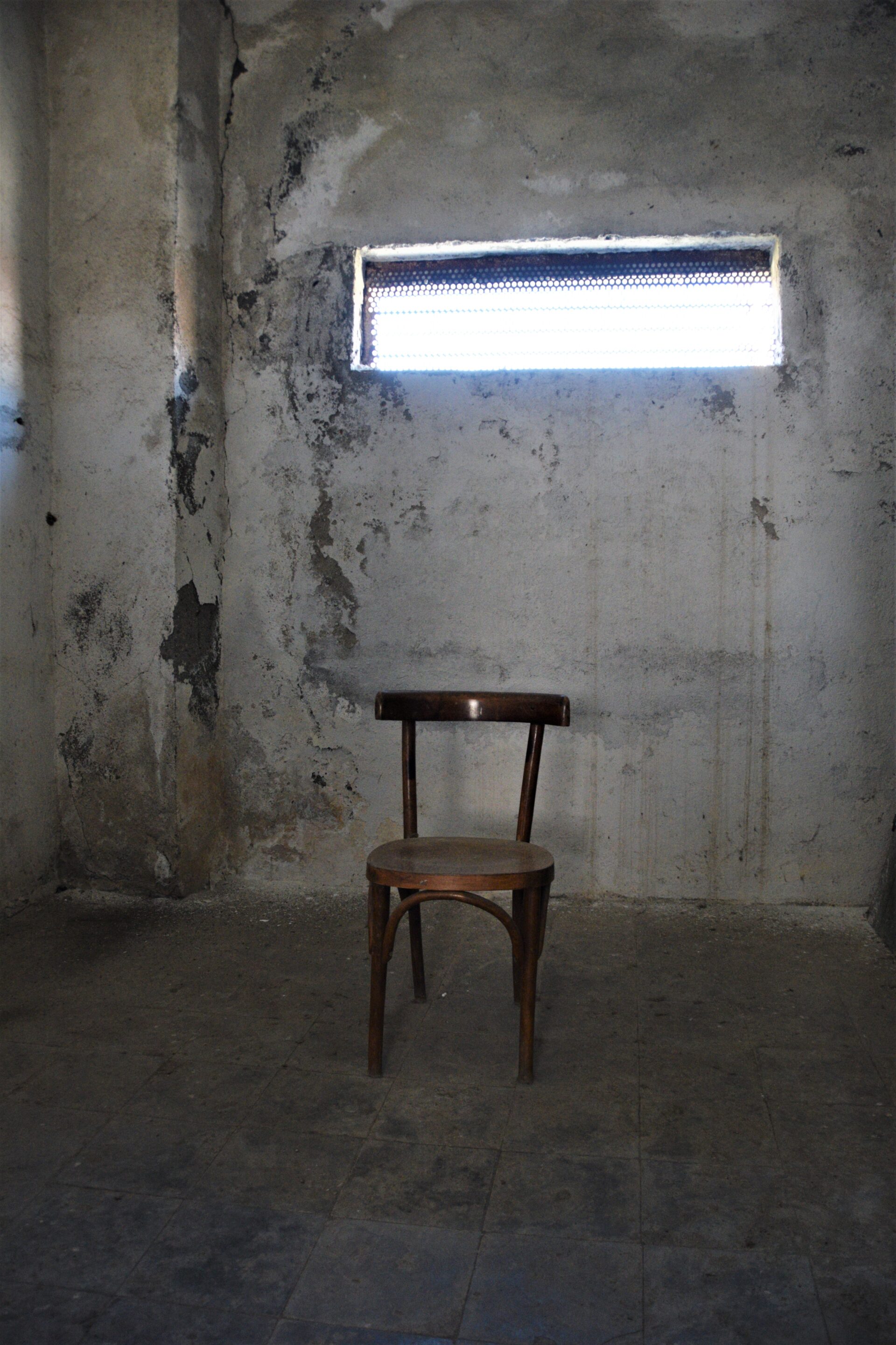 a single, wooden chair stands in the middle of a prison cell