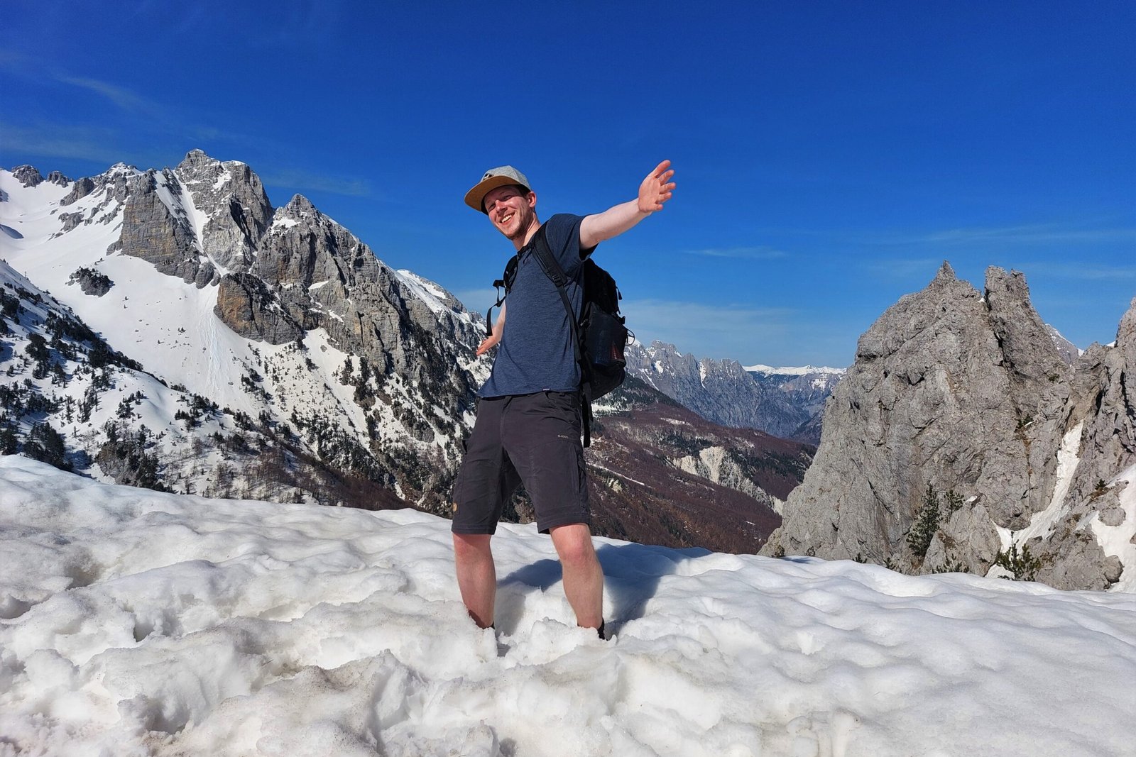 a man standing in the snow ony wearing shorts and a t-shirt, surrounded by a stunning mountain landscape