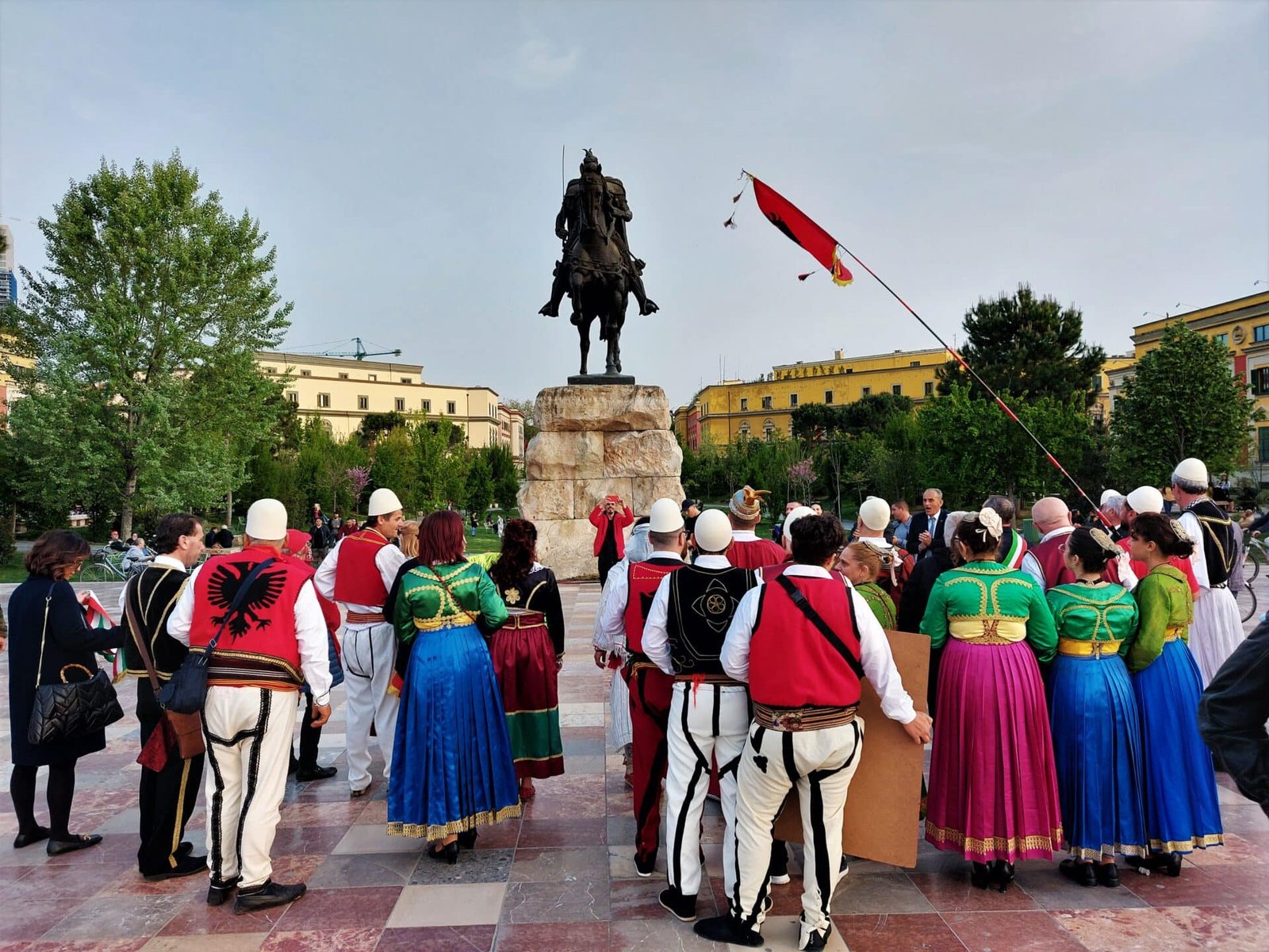 men and women dressed in traditional costumes in front of the Skanderbeg statue in Tirana