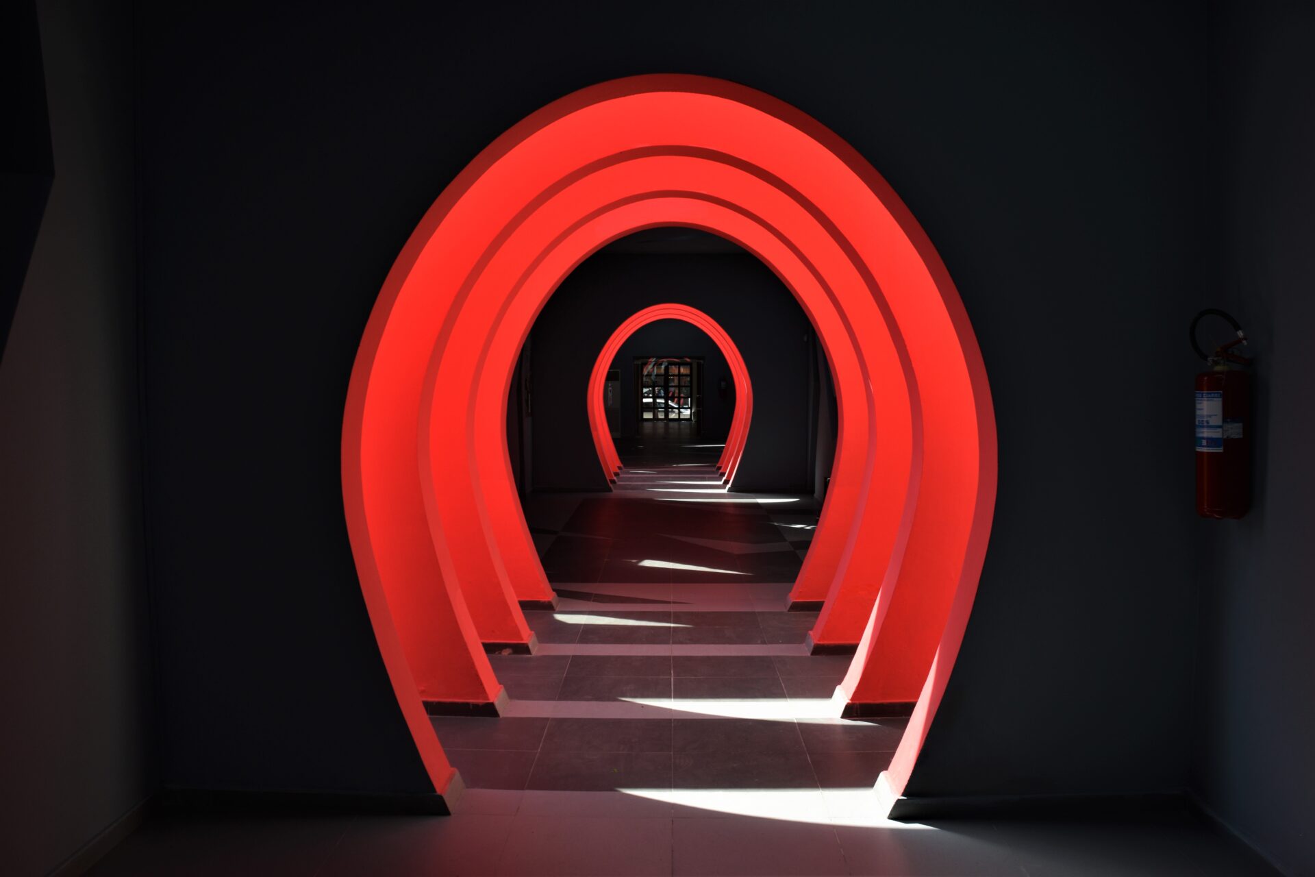 a dark hallway intersected by bright red arches