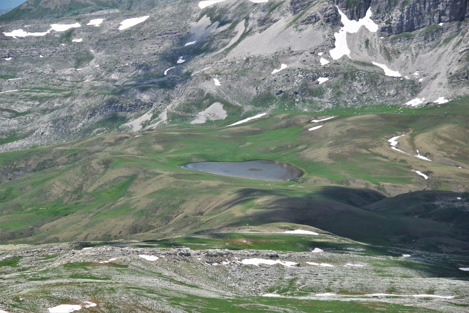 an alpine lake surrounded by green pastures in a rugged mountain landscape