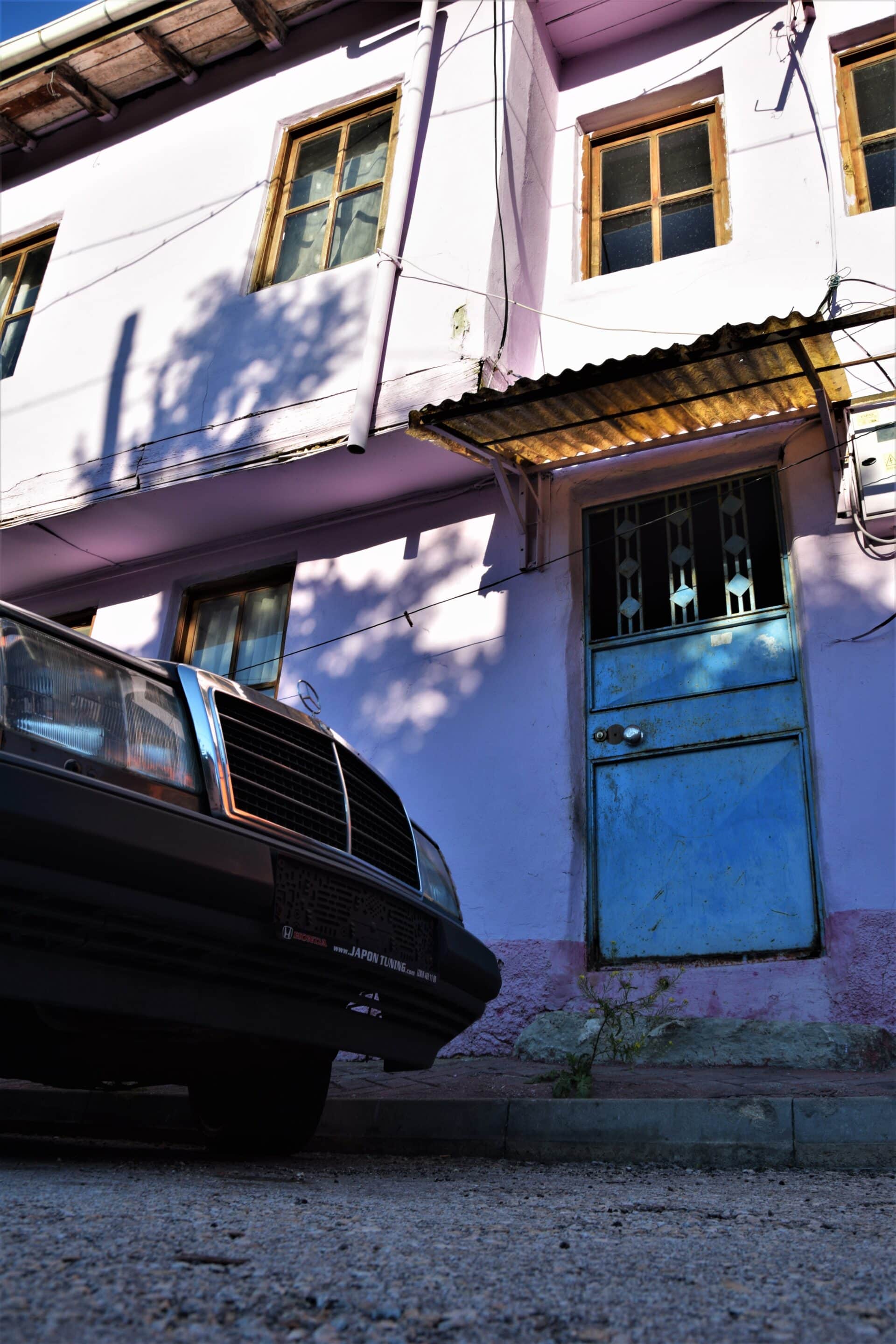 a grey car in front of a pink coloured building with a blue, metal door