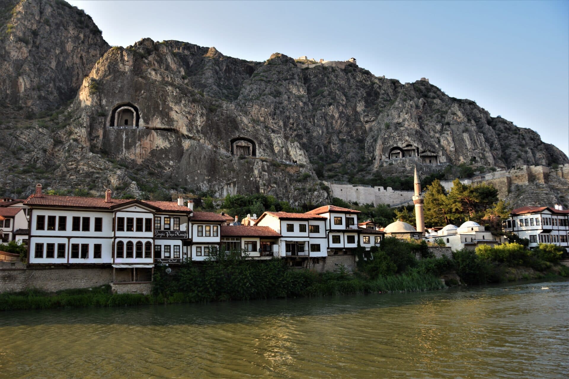 five monolithic rock tombs tower above whitewashed Ottoman-era buildings lining a river