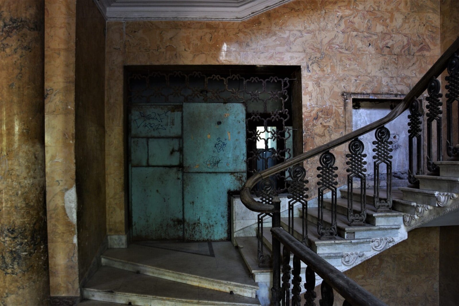 a staircase boasting a wooden railing leads to the second floor in front of a blue metal door in an old Soviet sanatorium