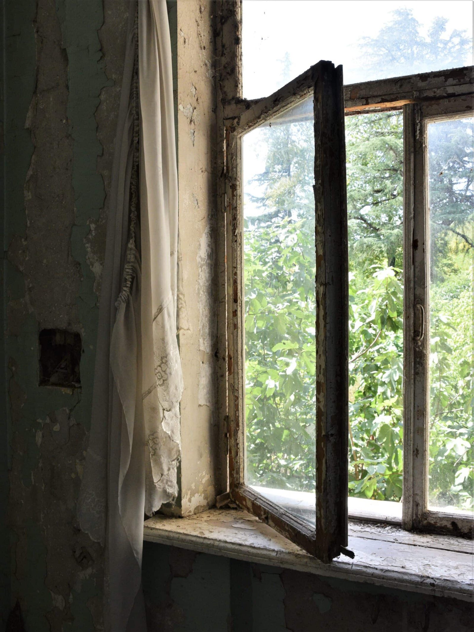 an old curtain hangs beside an open window in an abandoned sanatorium