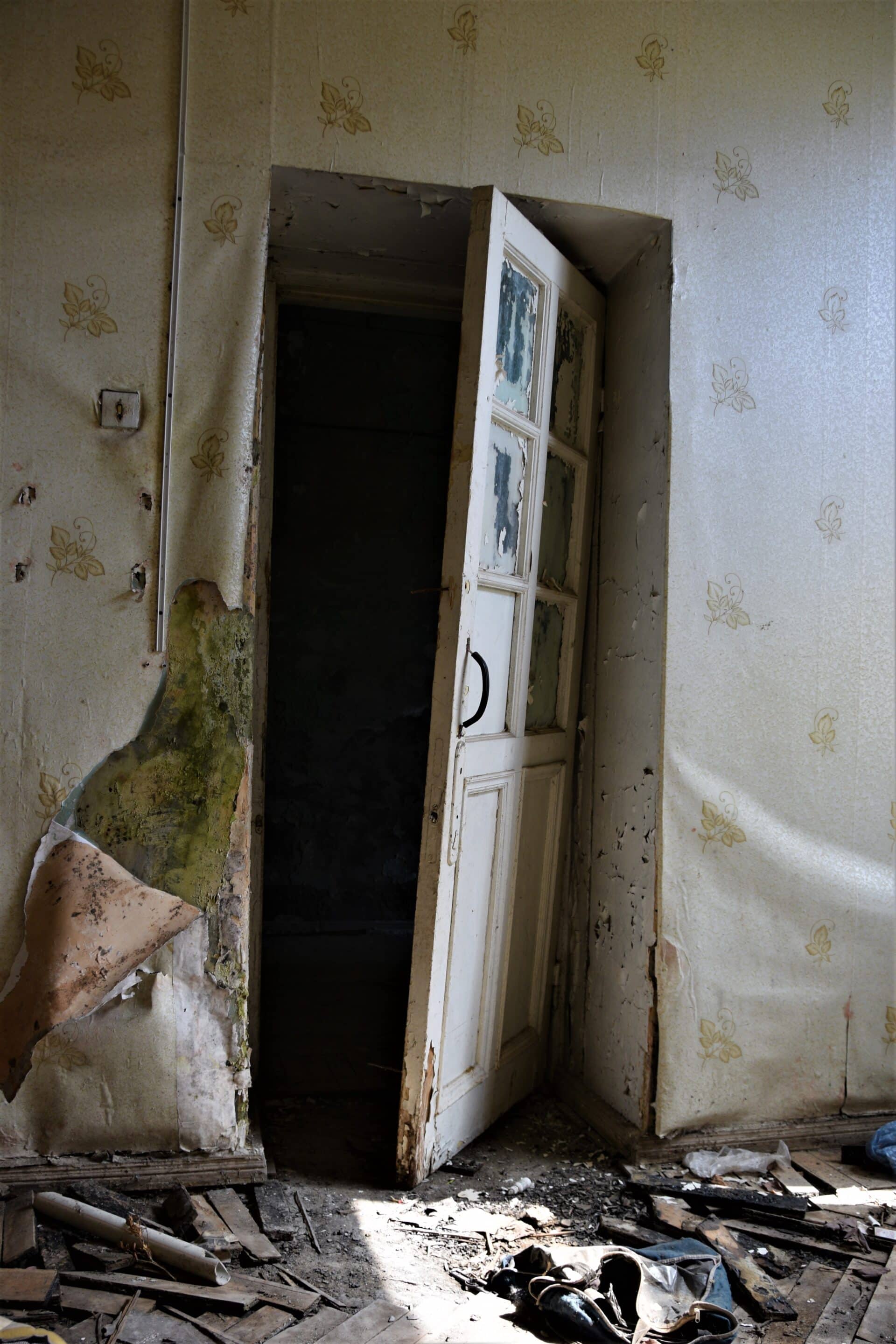 a white wooden door hangs on its hinges in an abandoned building