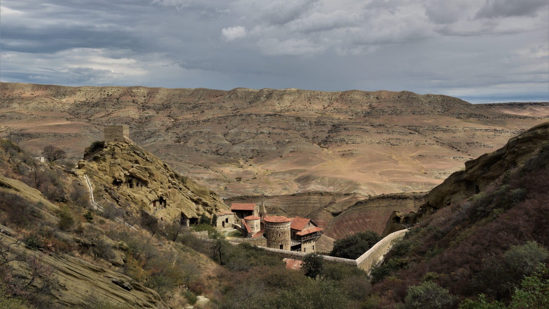 the dry hills of Georgia's southern steppe rise behind the red rooftops of David Gareja Monastery