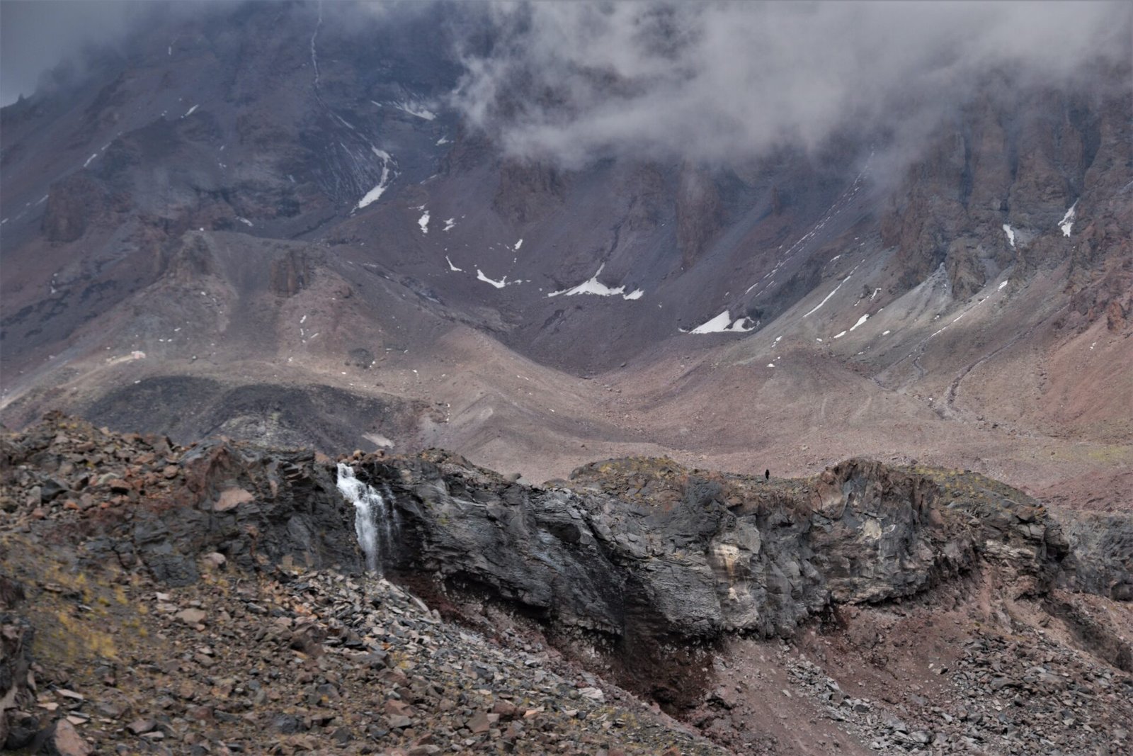 a hiker walking a long a cliffside below Gergeti glacier