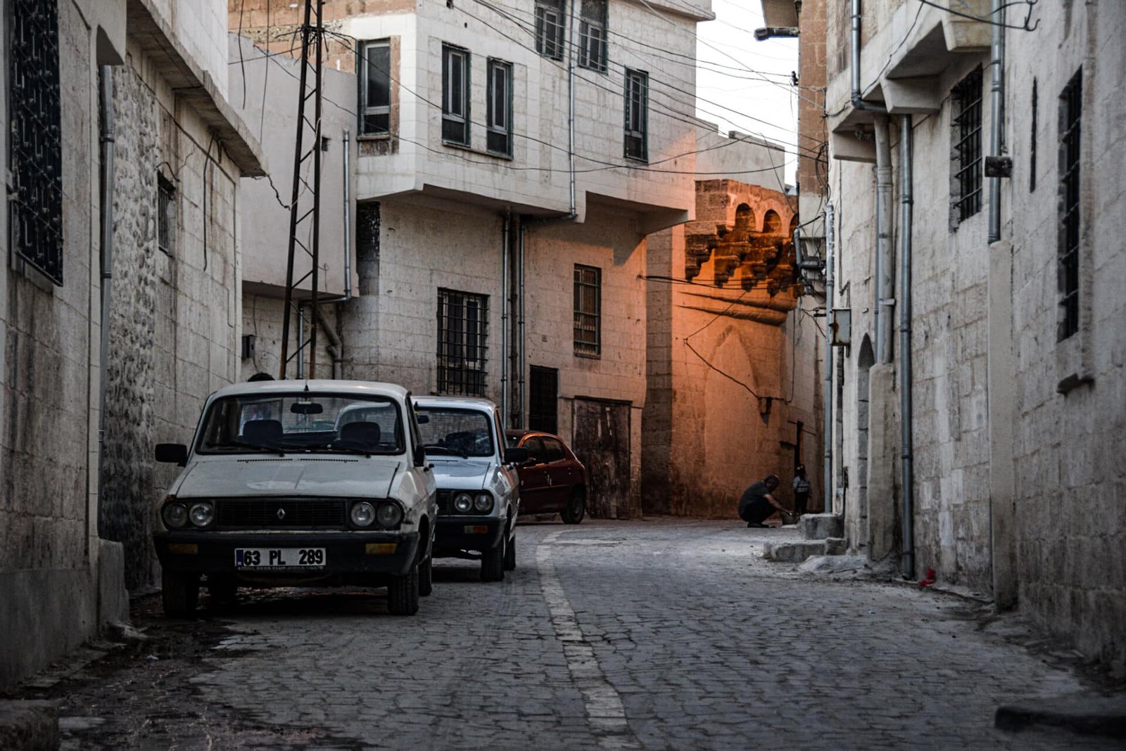 two old cars are parked on the left side of a cobbled street in Sanliurfa's old town