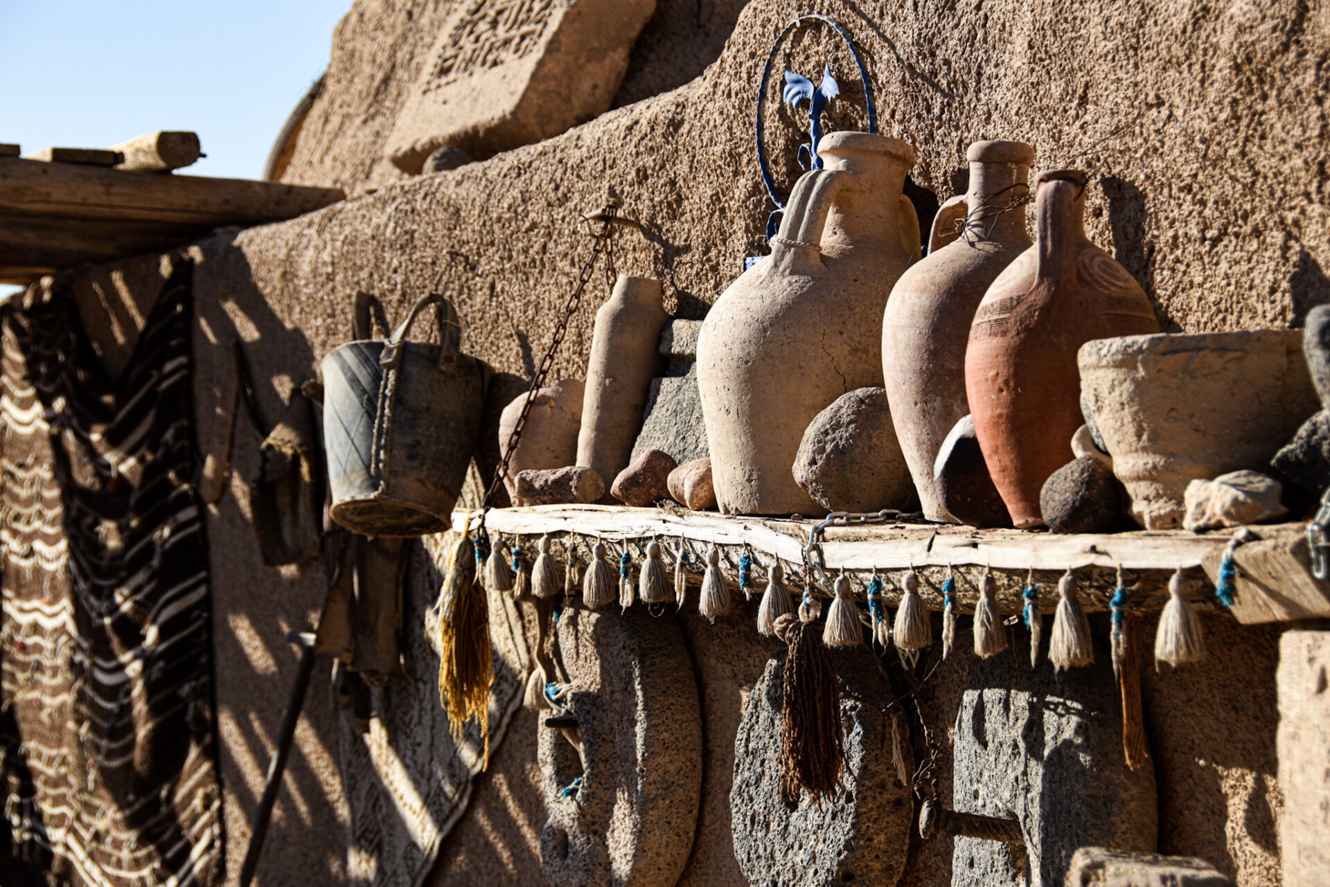 old ceramic jars sit on a wooden shelf on the outside of an adobe wall in Harran