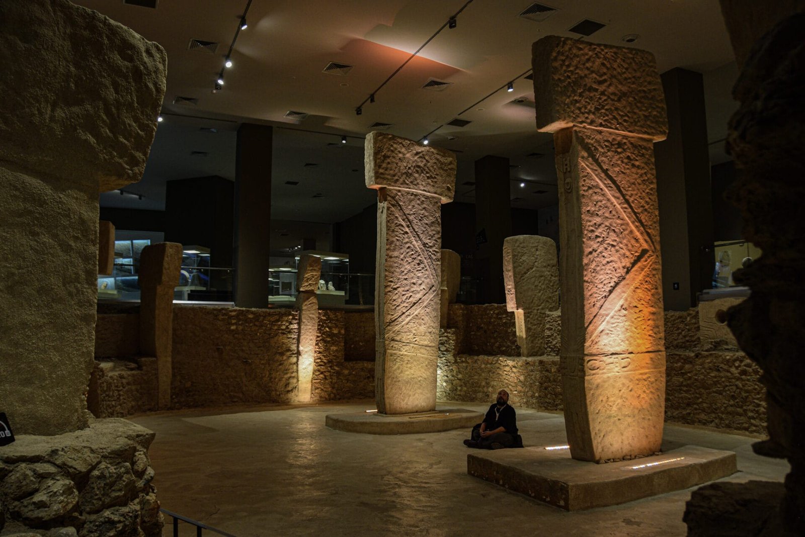a man sits on the floor between the life-size replicas of two giant t-shaped pillars from Göbekli Tepe in the Sanliurfa Archaeological Museum