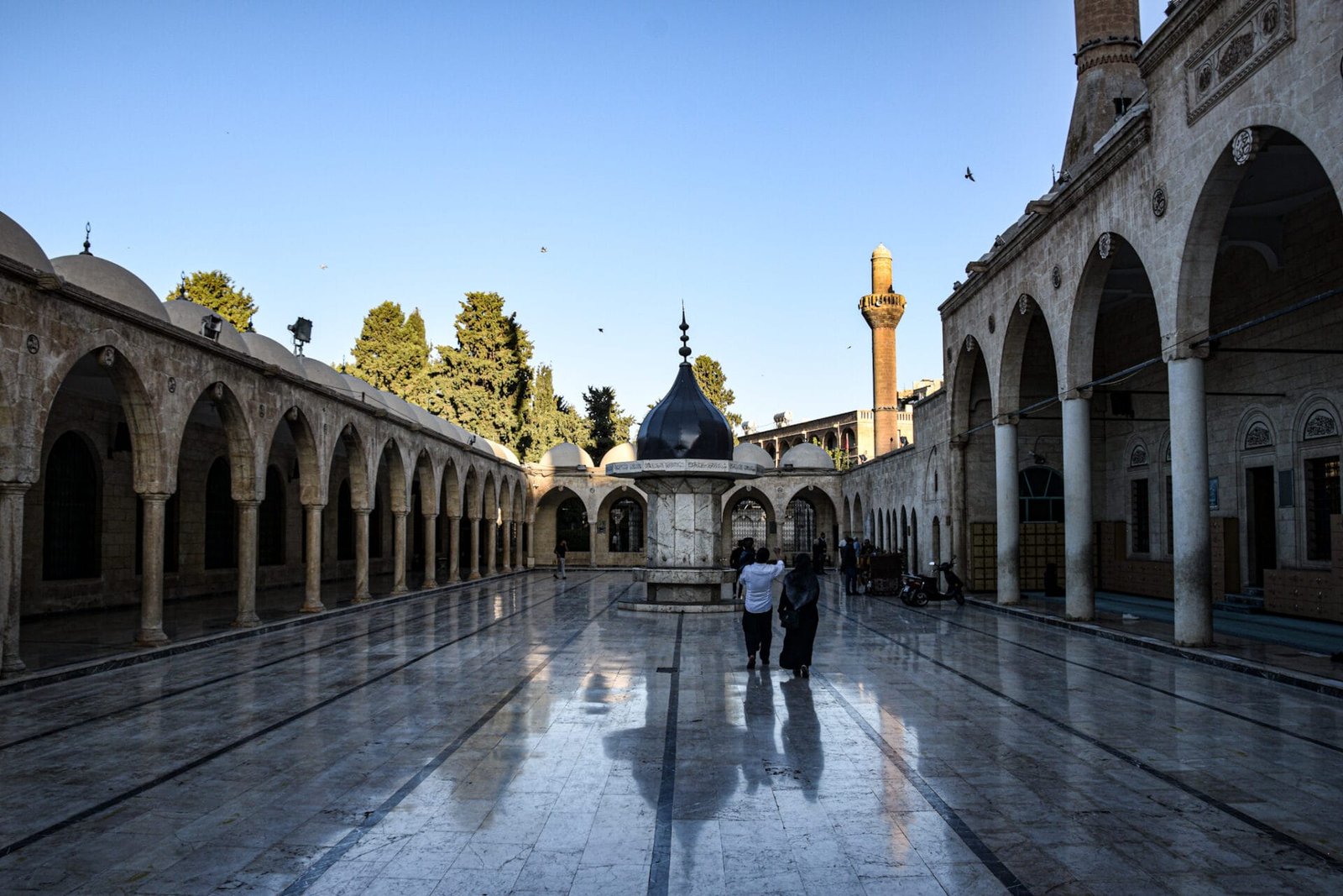 a family walks across the reflecting courtyard in front of a mosque