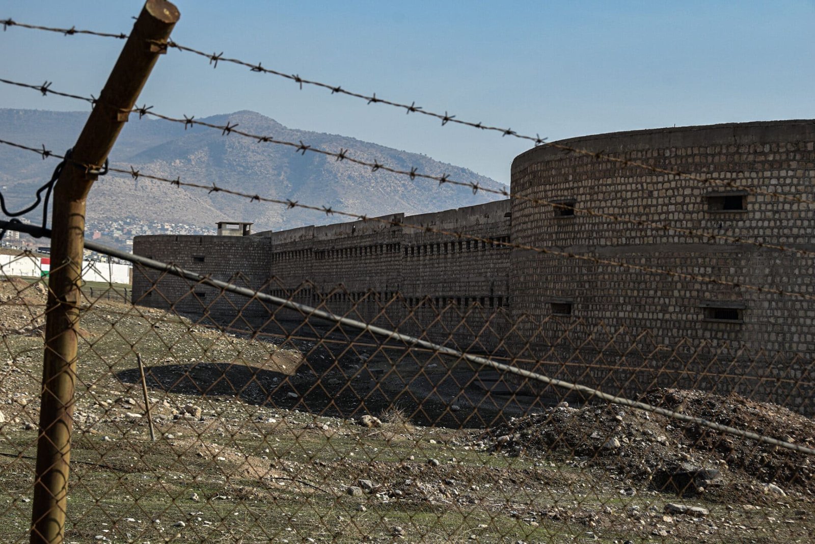 an abandoned Iraqi prison behind a rusted barbed-wire fence