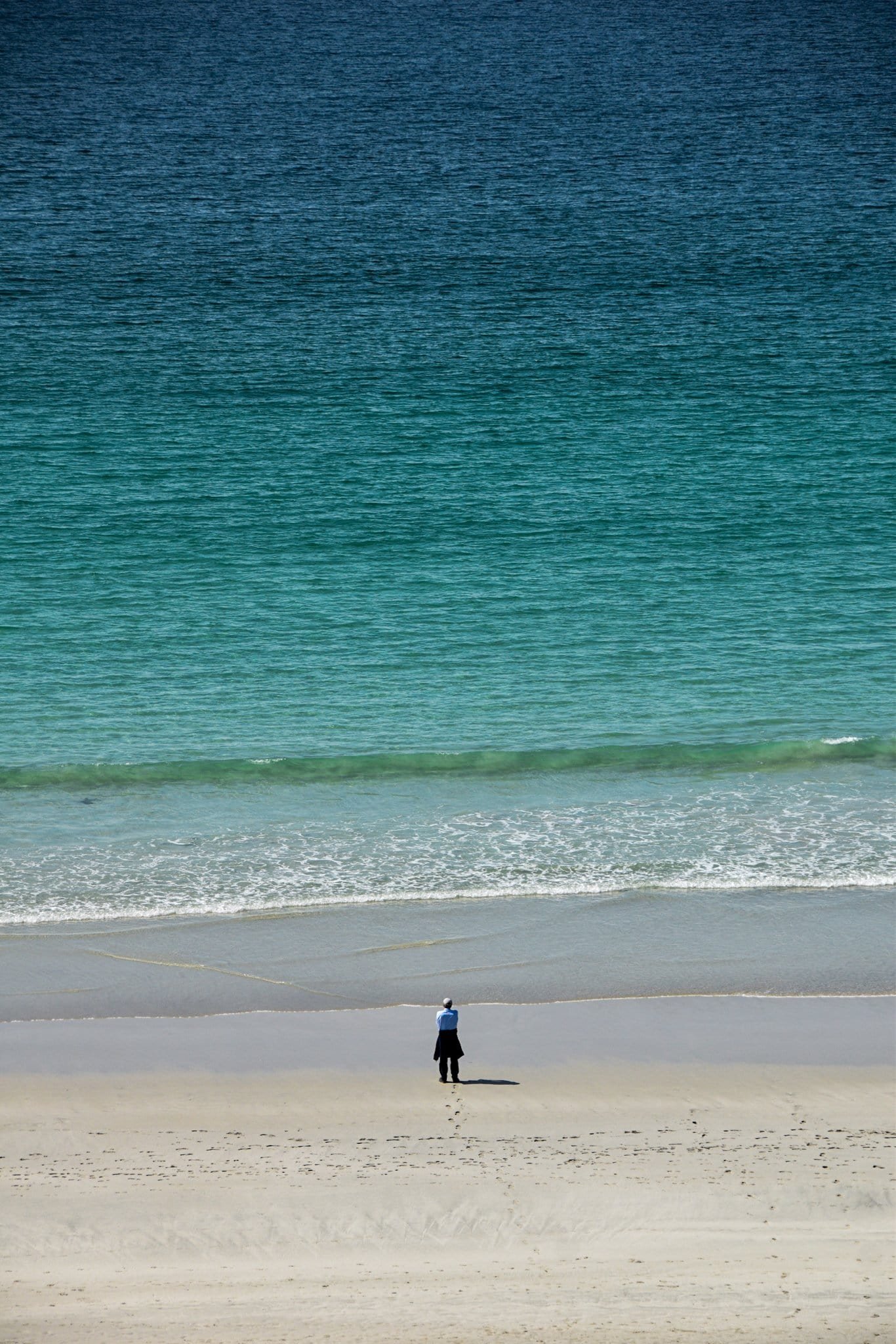 a man stands on the beach starring out to a deep turquoise sea