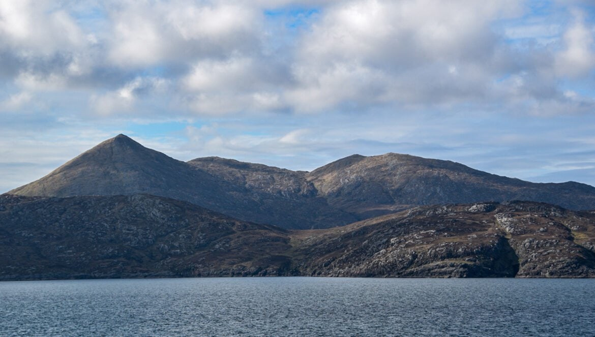 the rugged hills of Barra rise from the blue waters of the Atlantic