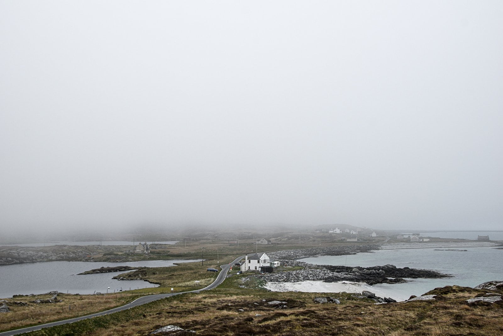 a white houses stands next to a country road vanishing in thick fog on the isle of South Uist