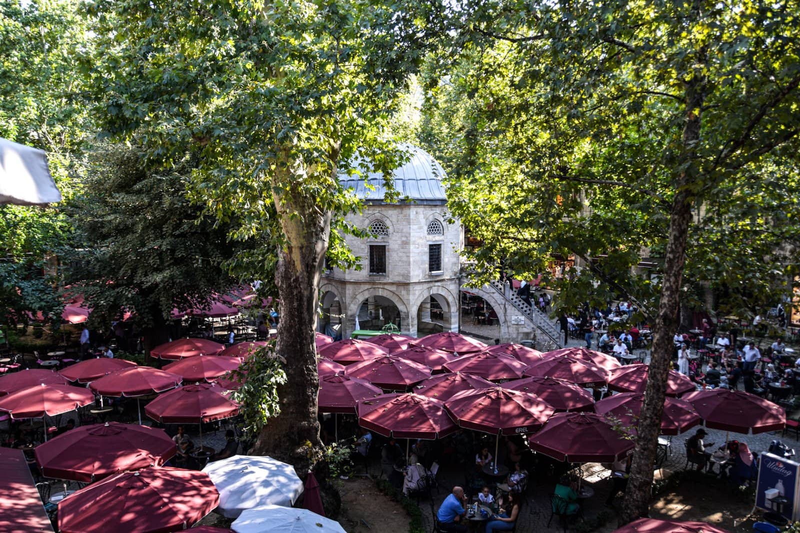 people sit under red umbrellas in the shaded yard of a Turkish han