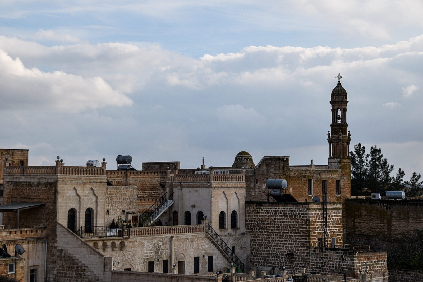 clouds tower over the level rooftops and minarets of Midyat