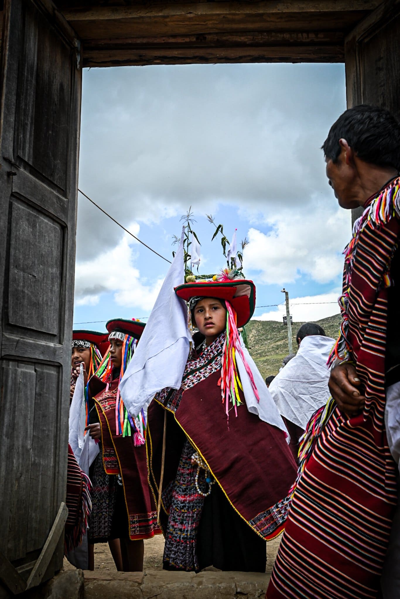 a girl dressed in the traditional dress of the Yampara people stands in a doorway