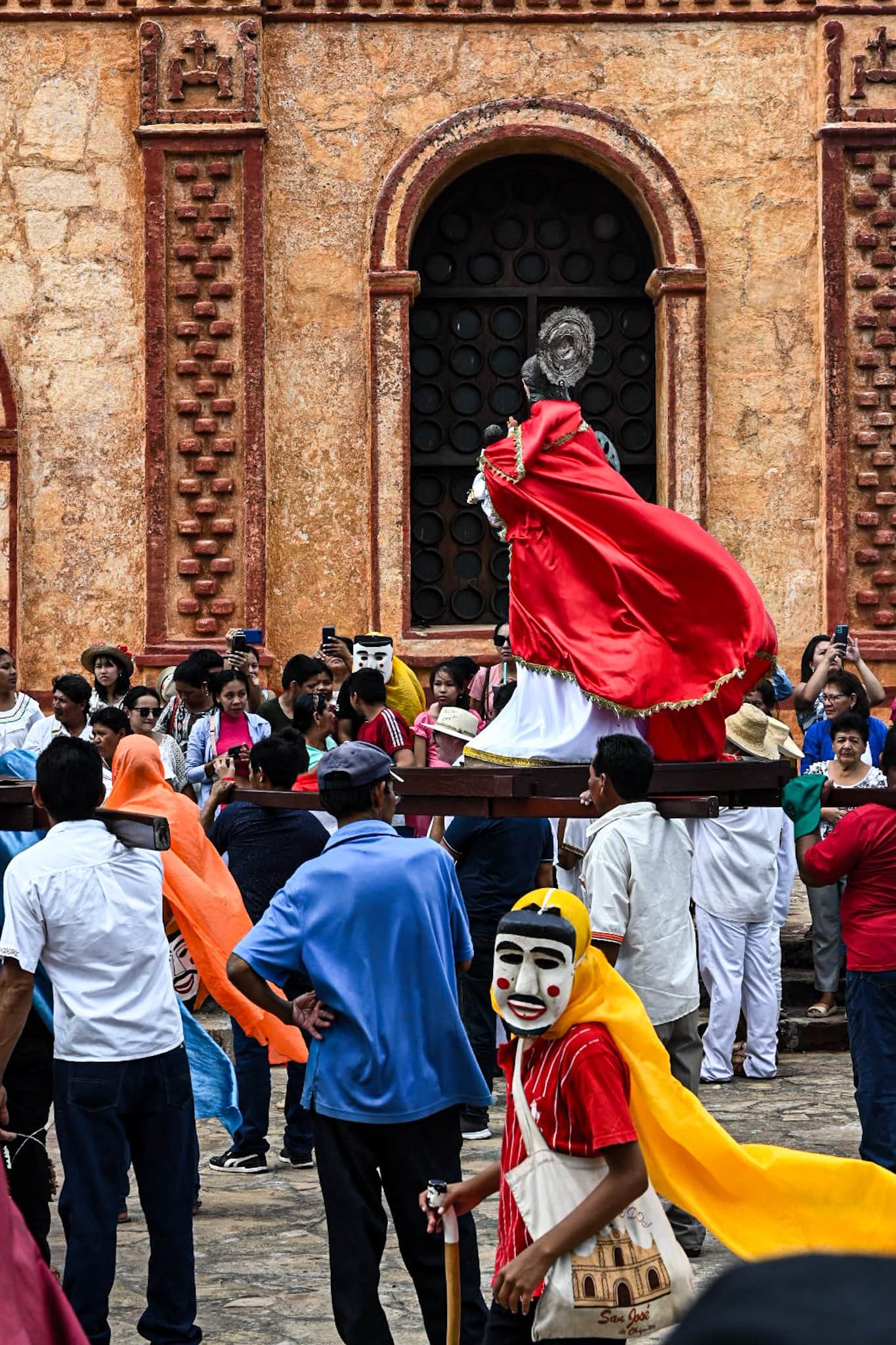 a crowd gathers in front of an old Jesuit church to witness a religious procession